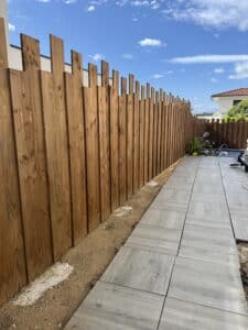 Clôture moderne en bois brun le long d'une allée carrelée grise en construction. Outils et ciel bleu avec nuages blancs. Aménagement extérieur.