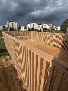 Plateforme en bois neuve avec balustrade, sous un ciel gris orageux. Des maisons modernes aux toits clairs se dressent en arrière-plan.